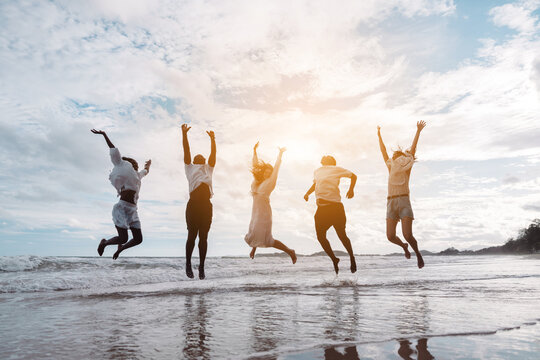 Happy diverse group of friends jumping on the beach, enjoying freedom, movement, and summer fun. active lifestyle, togetherness, and joyful friendship. - Powered by Adobe