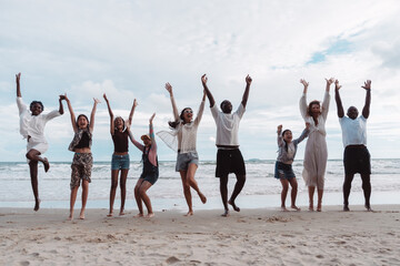 Happy diverse group of adults and children jumping together on the beach. Expressing family fun, freedom, vacation joy, and multicultural in nature.