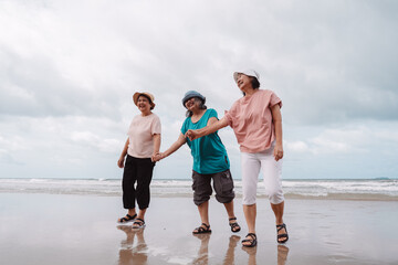 Asian elderly women enjoying a carefree moment on the beach, laughing and walking together along the shoreline. Concept of friendship, freedom, and joyful retirement lifestyle.