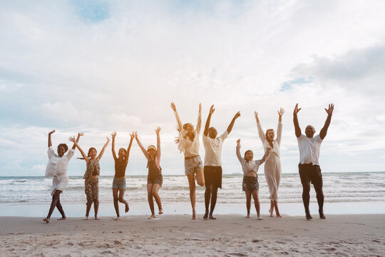 Happy family jumping together on the beach. Diverse group of adults and children celebrating togetherness, fun, joy and outdoor freedom. - Powered by Adobe