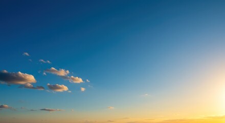 A panoramic view of a sunset sky, showcasing a vibrant gradient of deep blue transitioning to warm oranges and yellows near the horizon. 