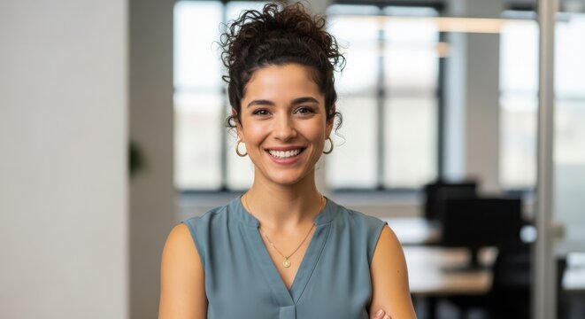 Woman with curly hair smiles and wears a blue sleeveless top and gold necklace female person