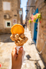Hand holding ice cream with narrow streets of the Old Town in Budva Montenegro in the background. Summer travel, local food, and vacation atmosphere.