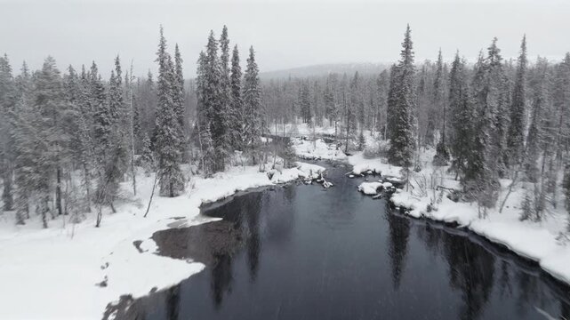 Aerial, slowly ascending flight above a river surrounded by snowy forest.