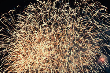 Large display of golden fireworks illuminates the night sky in a burst of celebration. Intricate patterns and sparkling trails