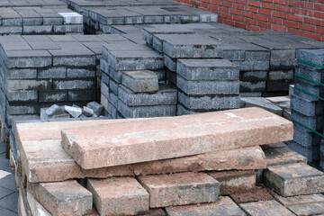 Konzept Baustelle Vorbereitung, Lieferung, Pause oder Baustopp: Unterschiedliche Pflastersteine auf Paletten gestapelt auf einem Grundstück vor einer roten Klinkerwand – selektiver Fokus, Textfreiraum
