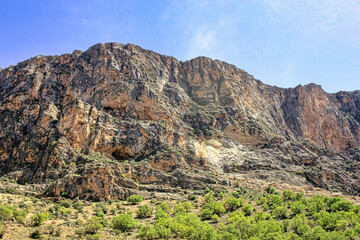 A mountain with a rocky cliff face and a green hillside