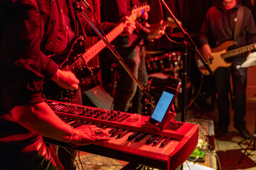 Live music performance with keyboard and electric guitar players on stage, lit by red stage...
