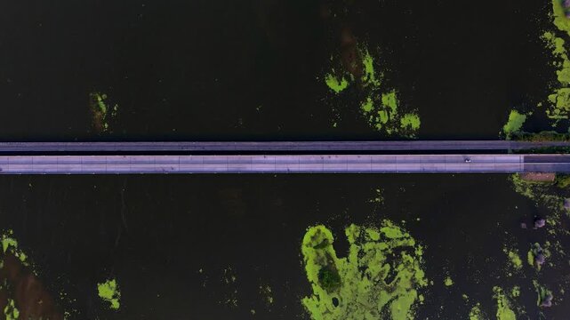 A unique aerial perspective of Chennai ECR's bridge over water, displaying light traffic and striking natural algae formations, a key scenic route. Very height aerial view of a bridge in Tamil Nadu