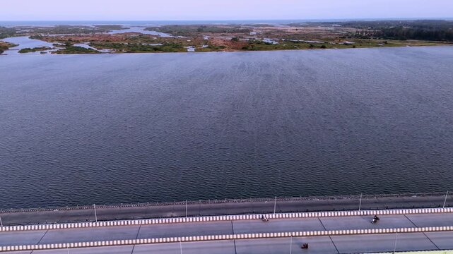 Aerial side view of a long bridge spanning a wide Palar River near Chennai, with distant wetlands and open sky, showcasing vital infrastructure. Palar river water mixing in ocean.