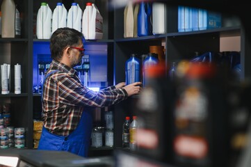 Salesman arranging engine oil bottles on shelf in auto parts store