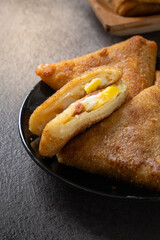 Close-up of Indonesian risoles filled with vegetables and mayonnaise, stacked on a black plate with stone surface background, showing golden crispy texture and savory filling in natural light