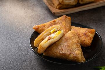 Close-up of Indonesian risoles filled with vegetables and mayonnaise, stacked on a black plate with stone surface background, showing golden crispy texture and savory filling in natural light