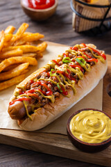 Juicy hot dog topped with minced meat, mustard, ketchup, and scallions on a soft bun, served with crispy fries and mustard dip on wooden tray over rustic table background in natural lighting