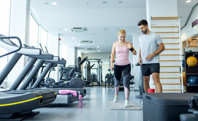 Personal fitness trainer supervising middle aged woman during gym workout.