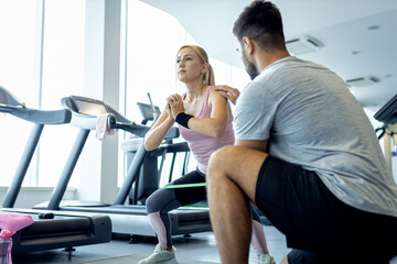 Personal fitness trainer supervising middle aged woman during gym workout.