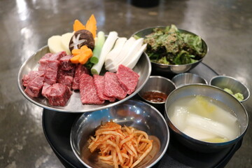 Korean Barbecue Grill Setup with Fresh Beef, Side Dishes, and Vegetables at Traditional Restaurant Table