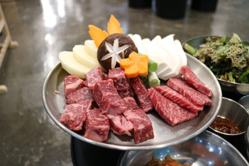 Korean Barbecue Grill Setup with Fresh Beef, Side Dishes, and Vegetables at Traditional Restaurant Table