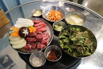 Korean Barbecue Grill Setup with Fresh Beef, Side Dishes, and Vegetables at Traditional Restaurant Table