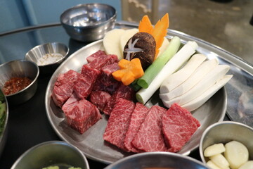 Korean Barbecue Grill Setup with Fresh Beef, Side Dishes, and Vegetables at Traditional Restaurant Table