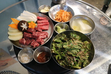 Korean Barbecue Grill Setup with Fresh Beef, Side Dishes, and Vegetables at Traditional Restaurant Table