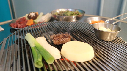 Korean Barbecue Grill Setup with Fresh Beef, Side Dishes, and Vegetables at Traditional Restaurant Table