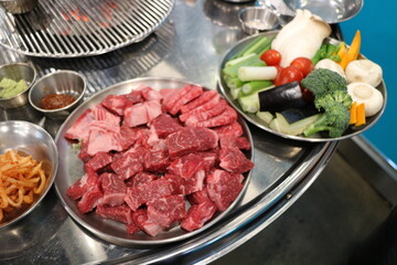 Korean Barbecue Grill Setup with Fresh Beef, Side Dishes, and Vegetables at Traditional Restaurant Table