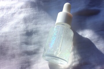 Clear iridescent serum dropper bottle on white fabric