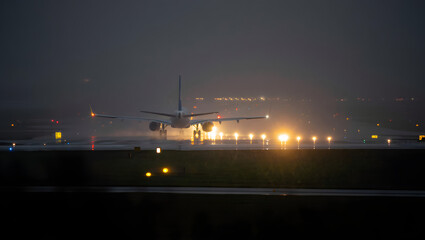 An airplane prepares for takeoff on a rainy night illuminated by runway lights
