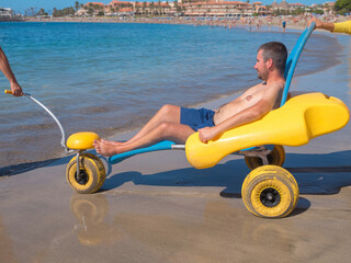 Person with disability using beach wheelchair enjoys time at an accessible beach. Gentle waves lap...