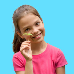 White girl in her 10s smiling and holding young mung sprout against blue background. Concept of sustainability, nature awareness, and childhood curiosity