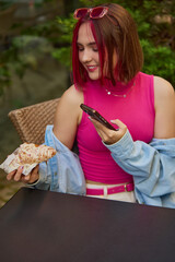 Young woman taking a picture with smartphone of a croissant at an outdoor cafe. Concept of social...