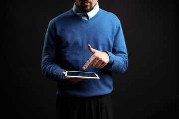 Man in blue sweater using tablet while standing against a dark background in a modern setting
