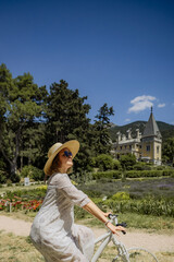 A woman is riding a bicycle in a park with a yellow house in the background