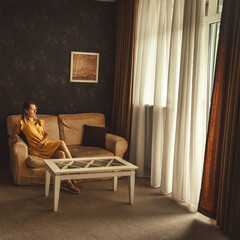 Young woman in yellow dress sitting on sofa