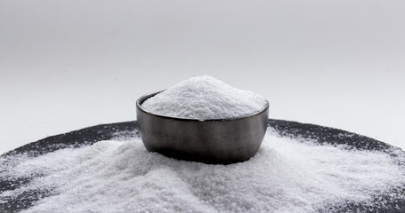 Iodized salt is in a metal container bowl, laying on a small pile of salt. Version I.