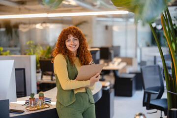 Young businesswoman holding clipboard smiling in modern green office