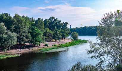 Obraz premium Lush green trees bordering Dnipro River channel in Kyiv with Rodina Mat visible in distance