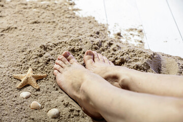 Close-up of bare feet resting on sand on beach wooden pier  in warm sunlight. The scene captures...