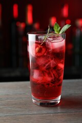 Tasty cherry soda water with ice cubes, berry and mint in glass on wooden table against blurred background, closeup