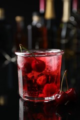 Tasty cherry soda water with ice cubes and berries in glass on mirror table against blurred background, closeup