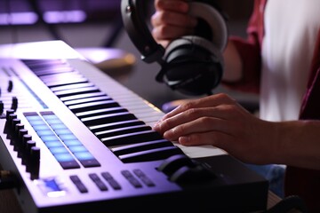 Man with headphones working with MIDI keyboard at table indoors, closeup