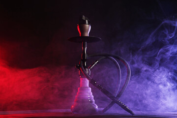 Hookah on wooden table with smoke in color lights against black background