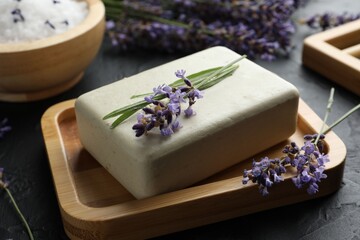 Aromatic soap bar and lavender flowers on dark textured table, closeup
