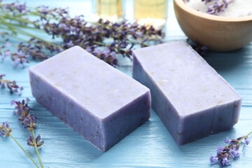 Aromatic soap bars and lavender flowers on light blue wooden table, closeup