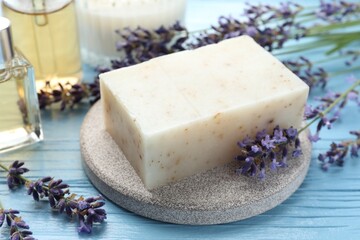 Aromatic soap bar and lavender flowers on light blue wooden table, closeup