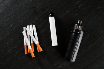 Electronic smoking devices and cigarettes on black table, flat lay