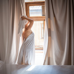 Young woman in a white towel standing by the window in the morning