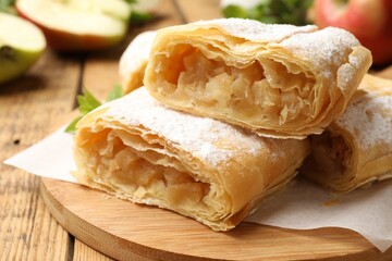 Pieces of tasty apple strudel with powdered sugar on wooden table, closeup