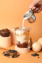 Woman pouring milk into bubble tea on orange background, closeup